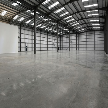 Empty industrial warehouse with polished concrete floors and steel framing.