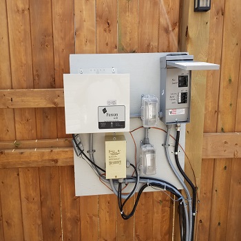 Pool control panel and electrical equipment mounted on wooden fence.