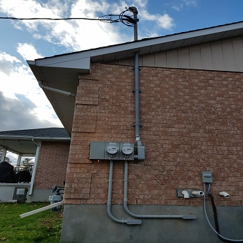 Exterior electrical meters and service conduit on brick home.