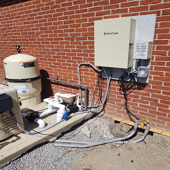 Pool pump and filtration system with Pentair control panel mounted on brick wall.