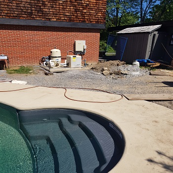 Pool equipment area beside pool deck with filtration and control units.