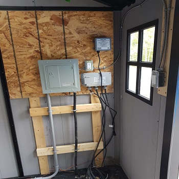 Electrical panel and control devices installed on interior shed wall.