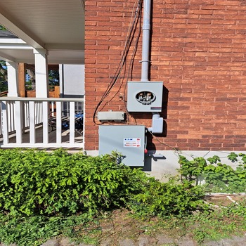 Exterior electrical service panel and meter mounted on brick wall.